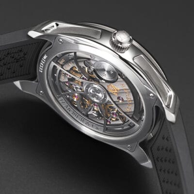 Eine Nahaufnahme einer Luxusuhr mit transparentem Gehäuseboden, der die komplizierten inneren Mechanismen offenbart. Die metallischen Komponenten, Zahnräder und Inschriften sind sichtbar und zeigen die im Uhrenlexikon beschriebene Handwerkskunst. Die Uhr hat ein schwarzes Armband mit strukturierter Oberfläche.