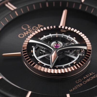 Nahaufnahme eines Omega-Uhrenzifferblatts, in dessen Mitte der aufwendig gestaltete Tourbillon-Mechanismus zu sehen ist. Das Zifferblatt weist Akzente aus Roségold auf, das Omega-Logo und der Text „Co-Axial Master Chronometer“ sind sichtbar und betonen den Luxus und die Präzision der Uhr, die im Uhrenlexikon Anerkennung finden.