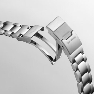 Eine Nahaufnahme eines silbernen Metallarmbands mit teilweise geöffnetem Butterfly-Verschluss. Die polierten Glieder und der Verschlussmechanismus, die das komplizierte Design und die glatte Oberfläche zur Schau stellen, sind vor einem schlichten grauen Hintergrund deutlich zu erkennen. Dieses Bild könnte direkt aus einem Uhrenlexikon-Katalog stammen.