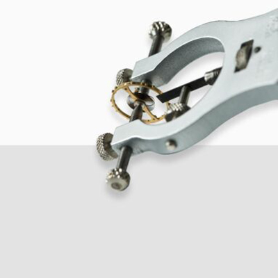 Nahaufnahme eines speziellen Uhrenlexikon-Werkzeugs, das ein kleines zahnradähnliches Bauteil auf einem weiß-grauen Hintergrund hält. Das Werkzeug scheint für Präzisionsarbeiten oder mechanische Einstellungen konzipiert zu sein.